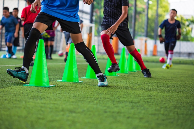 サッカーアカデミーでスキルを実行している子供たちを訓練するためのコーンと芝生のフィールドでのサッカーボールの戦術