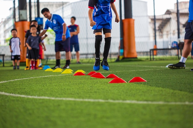 写真 サッカーアカデミーで子供たちのジャンプスキルを訓練するための障壁を持つ芝生のフィールドでのサッカーボールの戦術