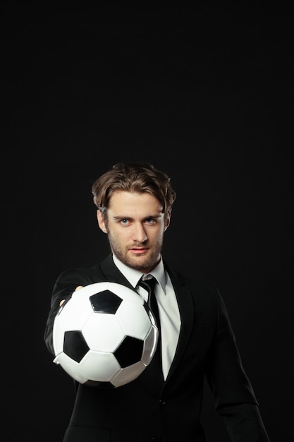 Soccer coach in black suit holding a ball