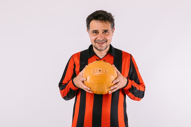 Photo soccer fan wearing a black and red striped jersey, holds a retro ball in his hands on white background