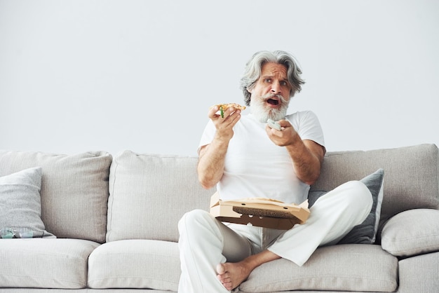 Soccer fan with pizza watches match Senior stylish modern man with grey hair and beard indoors