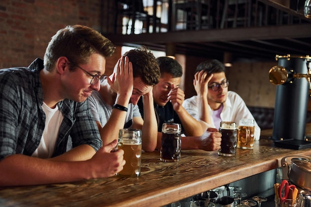 Photo soccer fans people in casual clothes sitting in the pub