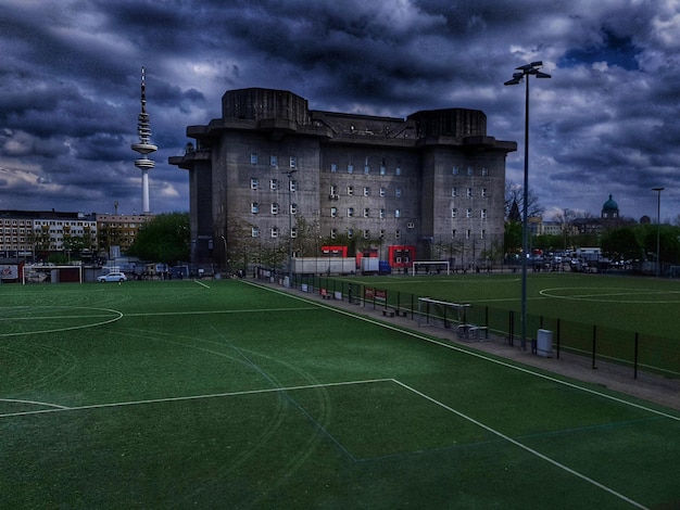 Soccer field by buildings against sky at dusk