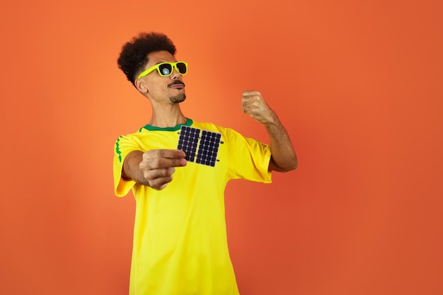 Soccer Player Black Man Celebrating Holding Solar Photovoltaic Panel Isolated on Orange Background