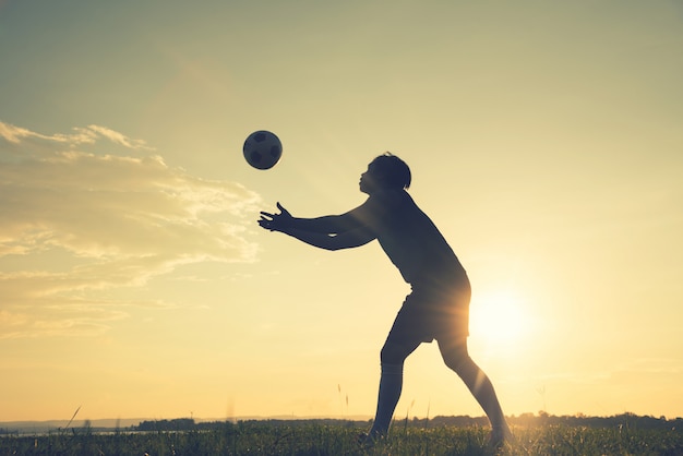 Uomo del calciatore che sta retrovisione in siluetta isolata sul fondo di tramonto