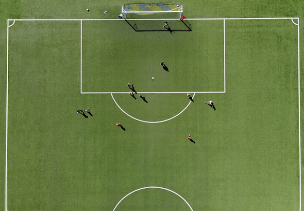 Soccer players playing a match on a green sports field viewed directly from overhead from a drone on a sunny summer day