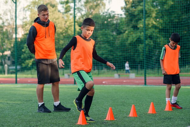 Soccer players running among plastic orange cones on artificial stadium