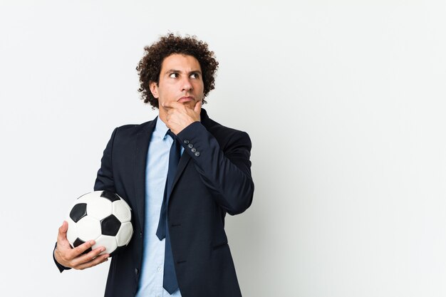 Soccer trainer holding a ball looking sideways with doubtful and skeptical expression.