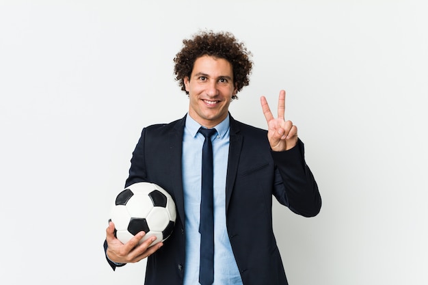 Soccer trainer holding a ball showing victory sign and smiling broadly.