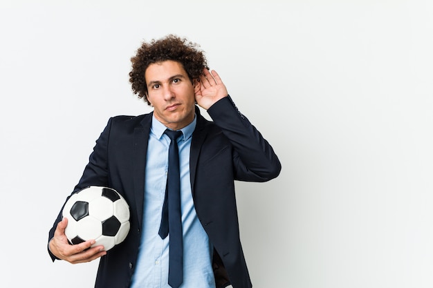 Soccer trainer holding a ball trying to listening a gossip