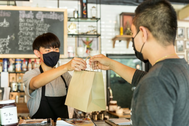 Foto cameriere concettuale di distanza sociale che dà borsa asportabile al cliente al caffè.