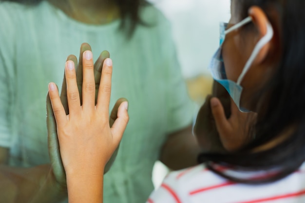 Social distancing among the family. Close up on hands of mother and daughter on a window plane. Stay at home during quarantine due to coronavirus COVID-19 pandemic.