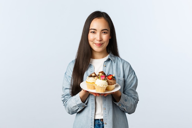 Stile di vita a distanza sociale, pandemia di covid-19, celebrazione delle vacanze durante il concetto di coronavirus. sorridente simpatico proprietario di un piccolo caffè che mostra cupcakes sul piatto e sorridenti, deliziosi dessert preparati.