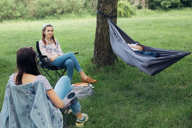 Social distancing Small group of people enjoying conversation at picnic with social distance in summer park Friends chilling in hammock and on chairs among trees