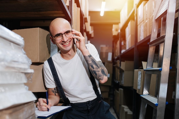 Social male warehouse worker talking on the phone writing on a clipboard