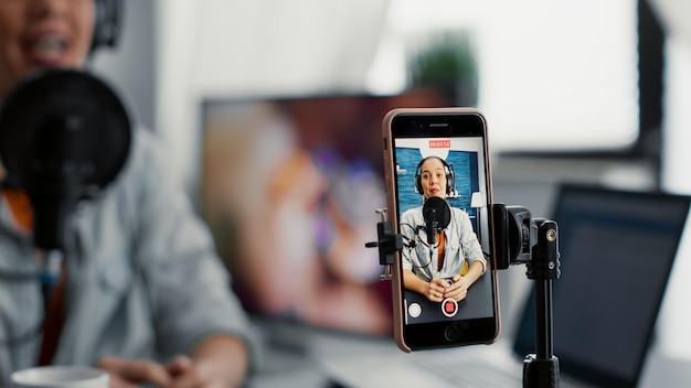 Photo social media content creator recording vlog with touchscreen phone while talking to audience. joyful internet star sitting at home studio desk while broadcasting video blog. close up