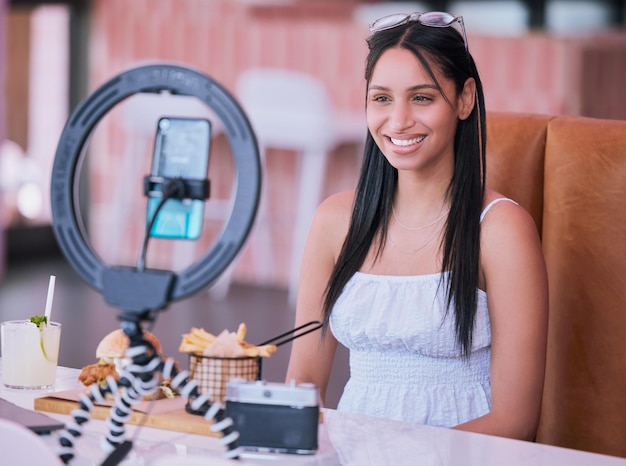 Social media influencer online video of food at cafe smartphone technology with mobile light lifestyle vlog Happy young girl in restaurant with film camera woman eating fries burger and cocktail