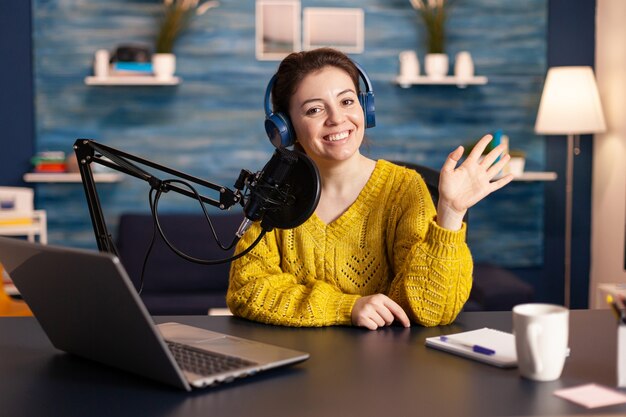 Social media influencer smiling at camera sitting in home studio ready for streaming new podcast ona...