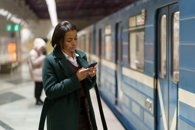 Sociale media verslaving Afrikaanse vrouw op metroplatform met smartphone surfen op internet in metro