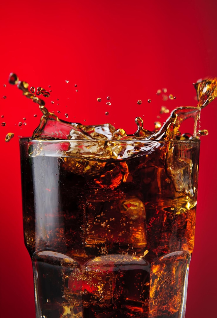 Photo soda on red with ice cubes splashing into the glass
