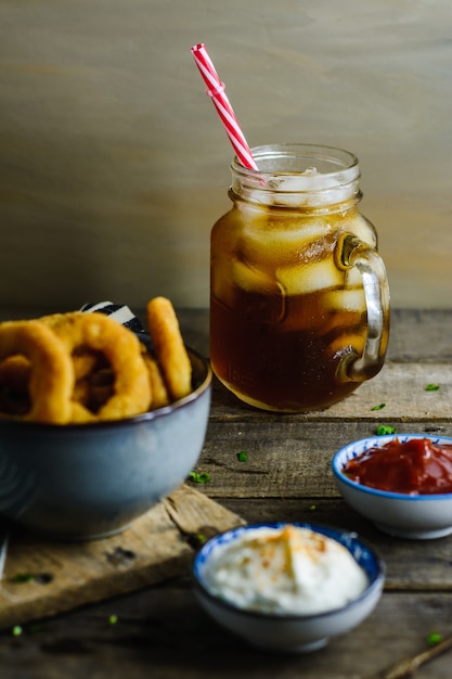 Soda surrounded by onion rings and sauces