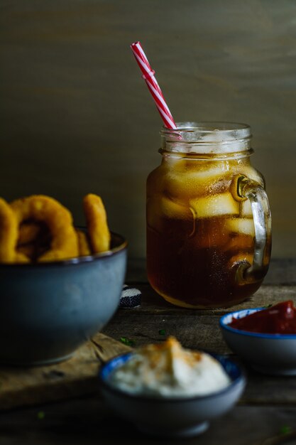 Soda surrounded by onion rings and sauces