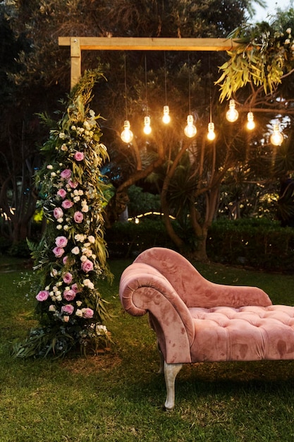 Photo sofa chaise lounge de terciopelo color rosado en un jardin con decoracion de flores y bombillas