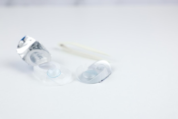 A soft blue contact lens sits on the edge of a disposable contact lens storage container next to it