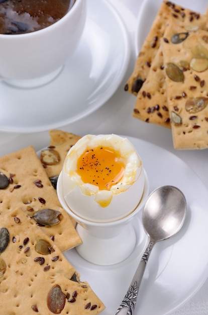 Soft-boiled egg with cup of coffee and crackers for breakfast