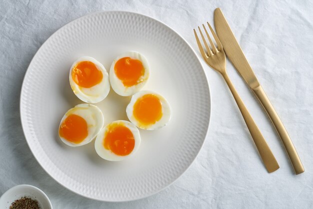 Soft-boiled eggs, peeled and cut into two halves, lying on white plate