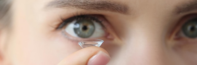 Soft contact lens on female finger against background of female eyes fitting daily lenses