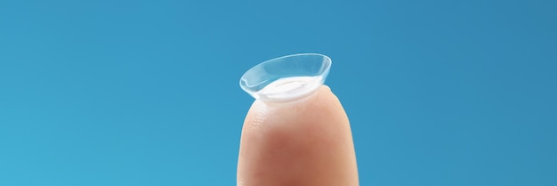 Soft contact lens on female finger on blue background. Fitting daily lenses concept