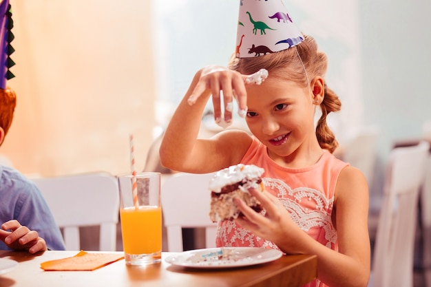 Crema morbida. piccola femmina allegra che mantiene il sorriso sul suo viso mentre va a mangiare la torta