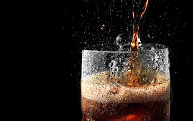 Soft drink glass with ice splash on dark background.