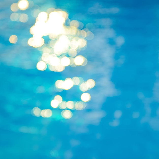 Soft focus bokeh light effects over a rippled blue water background in the pool