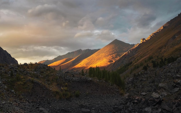 Мягкий фокус. Красочный горный пейзаж с большой горой, освещенной рассветным солнцем среди темных облаков. Потрясающие альпийские пейзажи с высокими вершинами горы на закате или на восходе солнца. Большая гора в оранжевом свете.