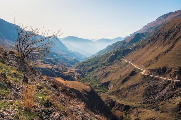 ソフトフォーカス。ダゲスタンの大きな岩山と壮大な深い峡谷のシルエットとカラフルな夕日の風景。山の端と急な崖に沿って運転する危険なオフロード。