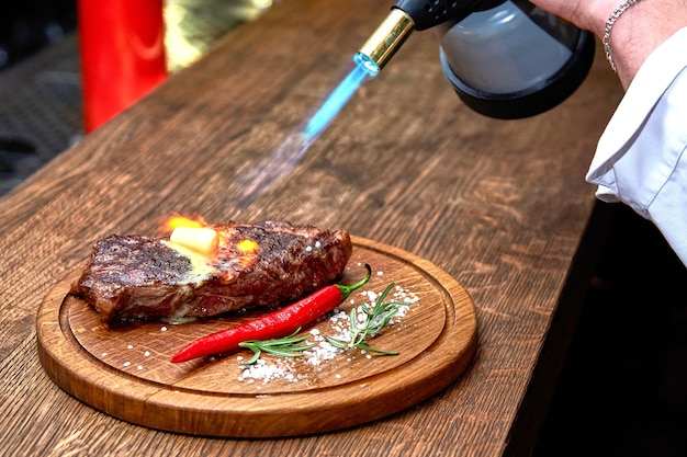 Focalizzazione morbida. entrecote manzo bistecca alla griglia con fiamme di fuoco su tagliere di legno con ramo di rosmarino, pepe e sale. master chef che cucina deliziosi barbecue alla griglia. sciogliere il burro