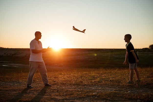 Soft focus of father and son playing toy airplane in meadow at sunset with happy emotions