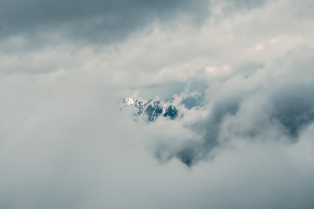 ソフトフォーカス。低い雲の上に大きな雪山の頂上がある素晴らしいミニマリストの風景。曇り空に大きな雪の山頂がある大気のミニマリズム。