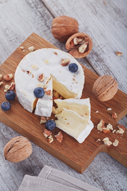 Formaggio francese a pasta molle di camembert servito con noci tritate e mirtilli su piatto di legno.