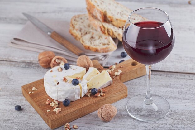 Soft french cheese of camembert served with chopped walnuts, glass of red wine and blueberries on wooden plate.