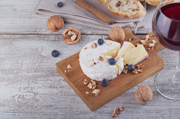 Soft french cheese of camembert served with chopped walnuts, glass of red wine and blueberries on wooden plate.