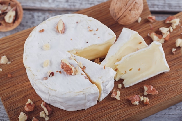 Soft french cheese of camembert served with chopped walnuts on wooden plate.