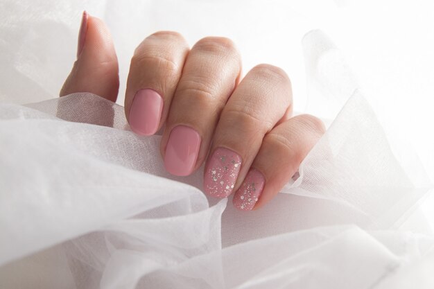 Vernice rosa tenue e scintillii sulle unghie - manicure con rivestimento in gel per salone.