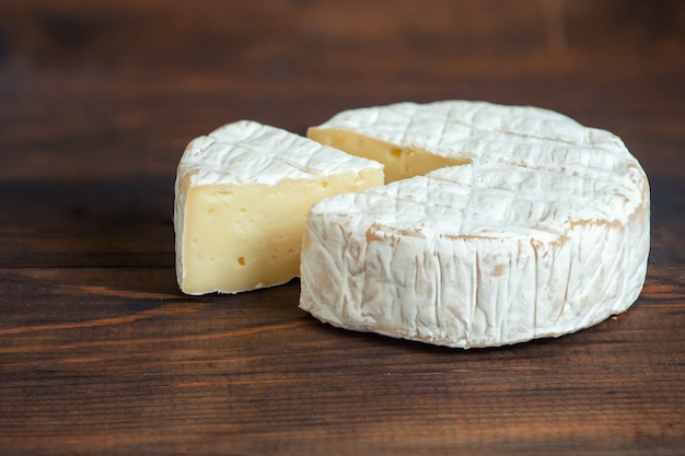 A soft ripened Camembert cheese on dark wooden board