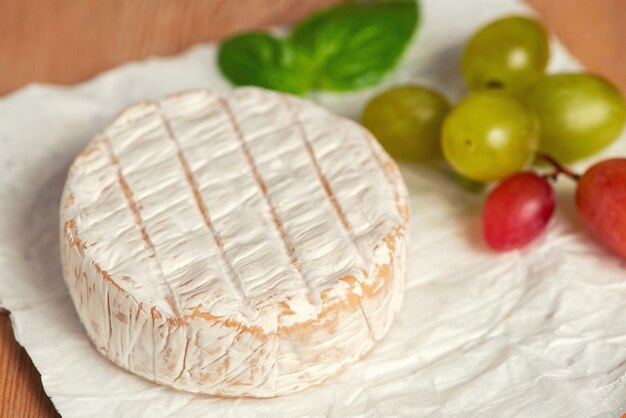 A soft ripened Camembert cheese and grapes on a white background