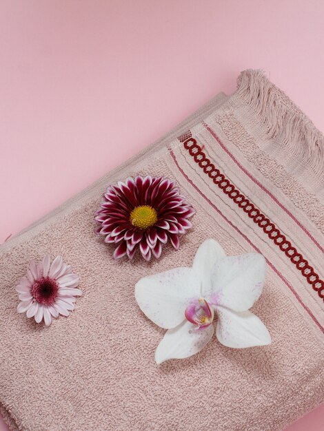 Мягкое махровое полотенце с белой орхидеей и бутонами на розовом фоне. Вид сверху.