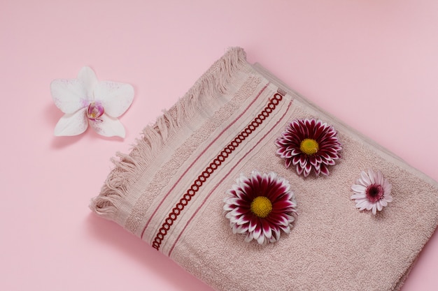 Soft terry towel with white orchid and red flower buds on pink background. Top view.