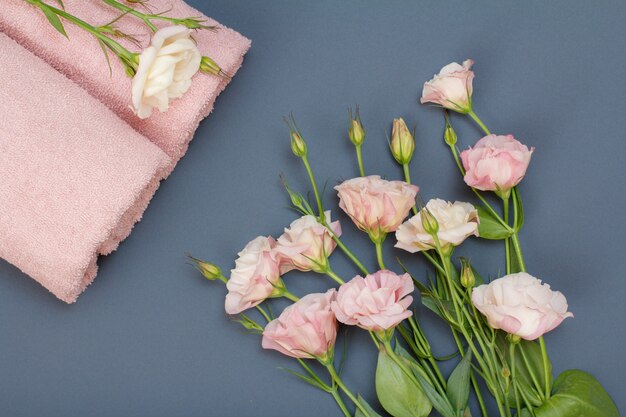 Soft terry towels with bouquet of pink rose flowers on gray background. Top view.